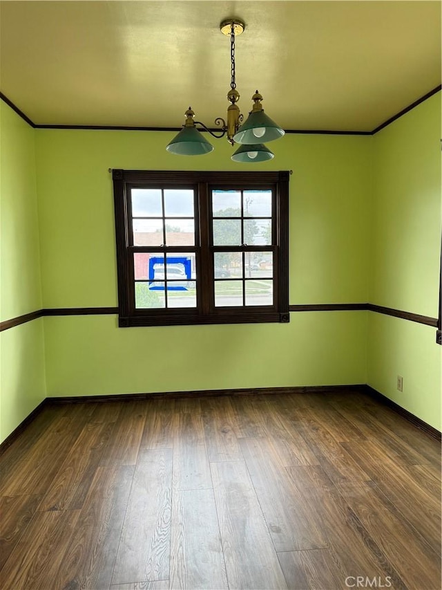 unfurnished room featuring a notable chandelier, crown molding, dark wood finished floors, and baseboards