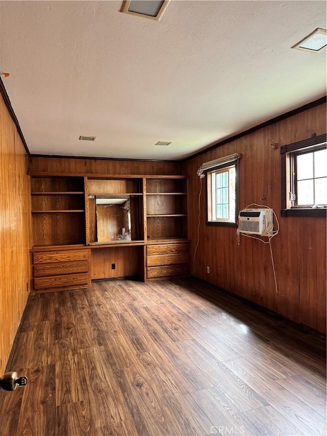 unfurnished living room featuring a textured ceiling, wooden walls, dark wood-style flooring, a wall mounted AC, and crown molding