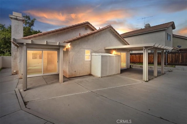 back of property at dusk with a patio area, stucco siding, a pergola, and fence