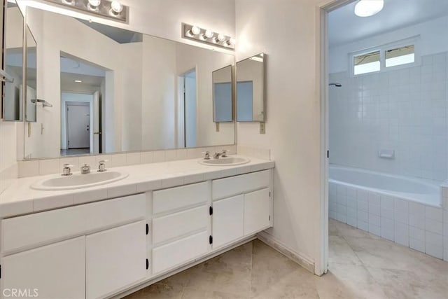 full bath featuring double vanity, baseboards, tiled shower / bath, and a sink