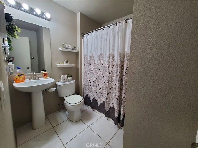 bathroom with tile patterned floors, a shower with curtain, toilet, a sink, and a textured wall