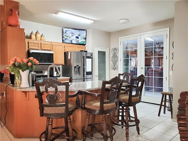 kitchen with a kitchen breakfast bar, appliances with stainless steel finishes, a peninsula, french doors, and light tile patterned flooring