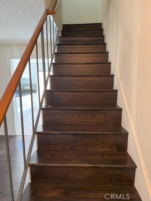 stairway with a textured ceiling and wood finished floors