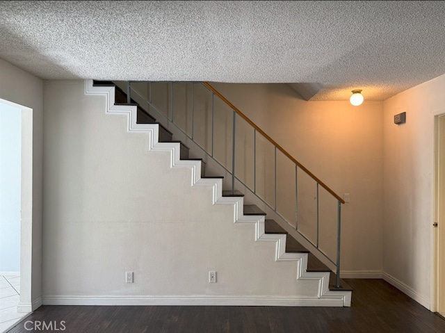 staircase featuring a textured ceiling, baseboards, and wood finished floors