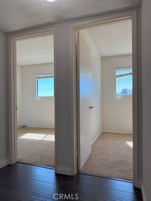 hall with a textured ceiling, plenty of natural light, and dark wood finished floors