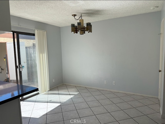 unfurnished dining area with tile patterned flooring, a textured ceiling, baseboards, and an inviting chandelier