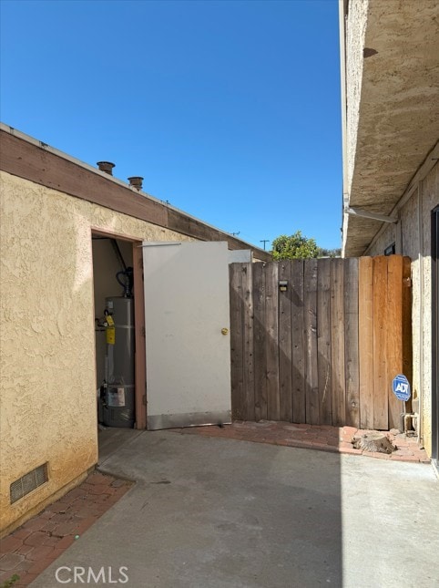 view of patio / terrace with water heater, fence, and visible vents