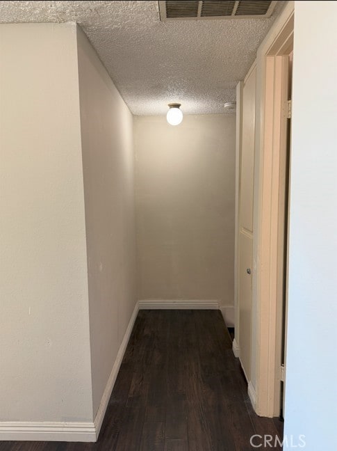 hall featuring a textured ceiling, wood finished floors, visible vents, and baseboards