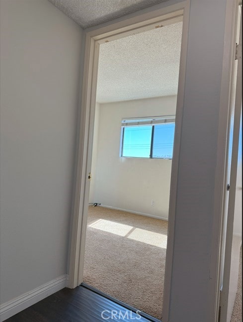 corridor featuring a textured ceiling, dark wood-style flooring, dark carpet, and baseboards