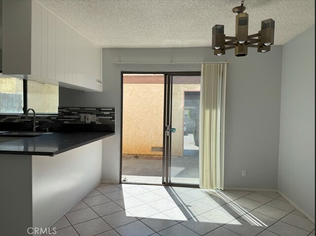 kitchen featuring light tile patterned floors, tasteful backsplash, dark countertops, a notable chandelier, and a sink