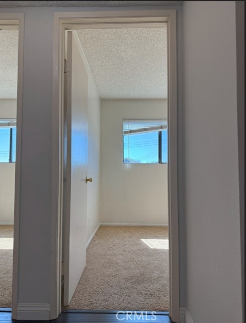 corridor with a textured ceiling, carpet, and baseboards