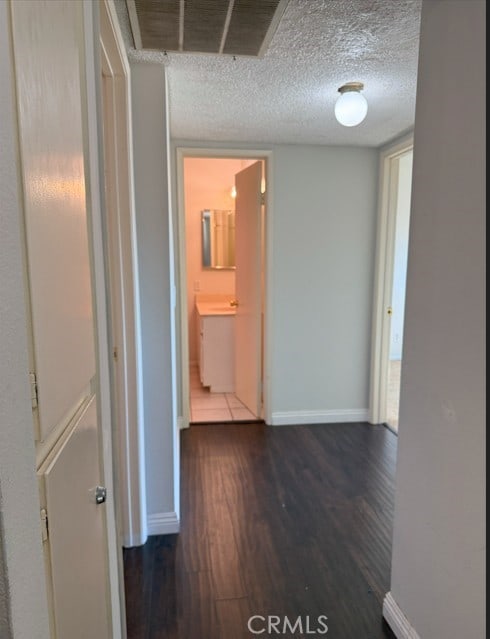 hall featuring dark wood-style floors, visible vents, baseboards, and a textured ceiling