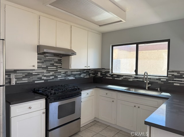 kitchen with light tile patterned floors, stainless steel gas range oven, under cabinet range hood, a sink, and dark countertops