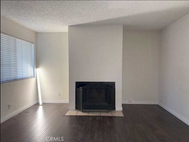 unfurnished living room with a fireplace with flush hearth, a textured ceiling, baseboards, and wood finished floors