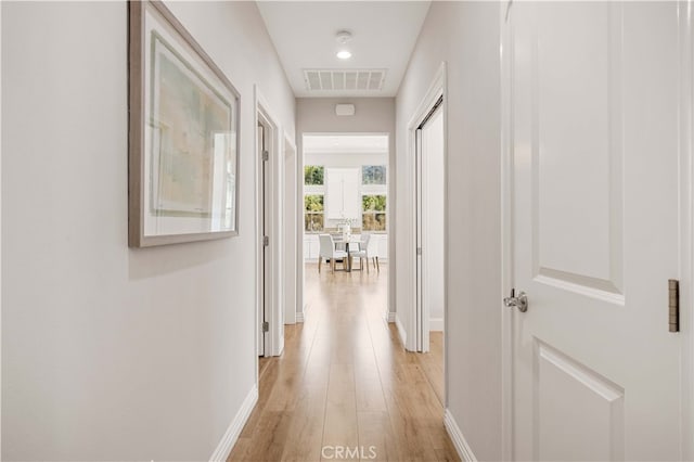 corridor featuring light wood finished floors, baseboards, and visible vents