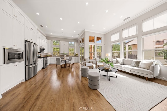 living area featuring ornamental molding, light wood finished floors, visible vents, and a healthy amount of sunlight