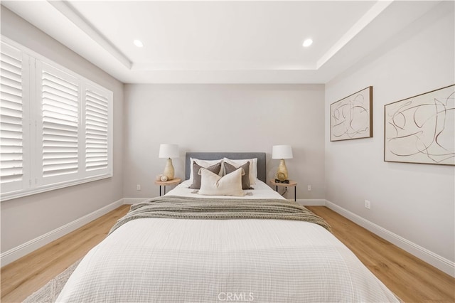 bedroom featuring light wood-style floors, baseboards, a raised ceiling, and recessed lighting