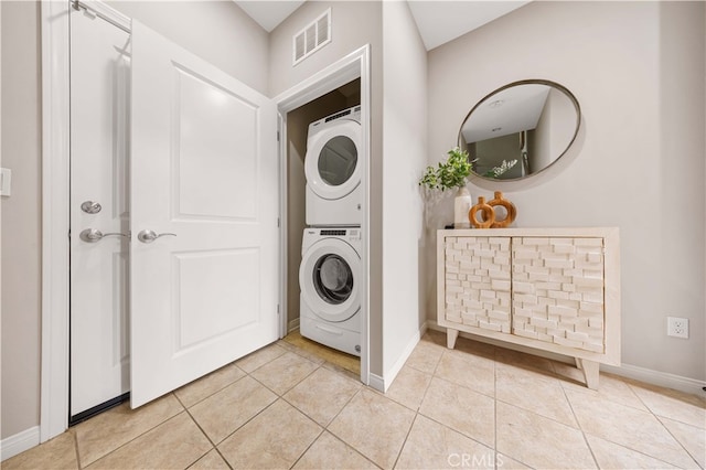 laundry area featuring stacked washer / dryer, light tile patterned flooring, visible vents, and baseboards