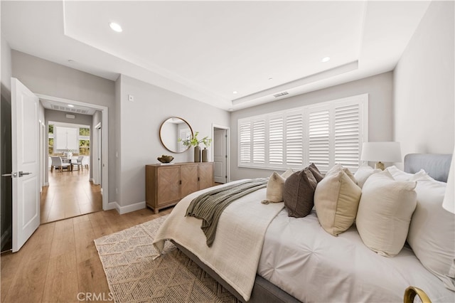 bedroom with visible vents, baseboards, light wood-style flooring, a tray ceiling, and recessed lighting