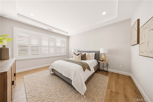 bedroom featuring light wood finished floors, recessed lighting, a raised ceiling, and baseboards