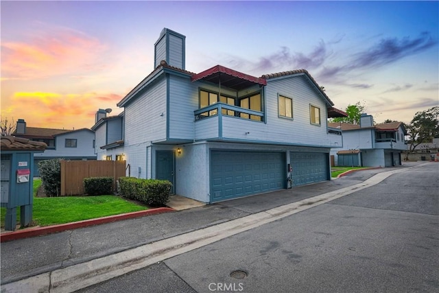 view of front of home featuring a balcony, a garage, fence, stucco siding, and a chimney