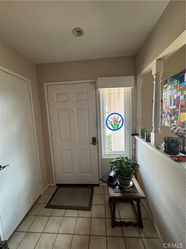 entryway with light tile patterned flooring, decorative columns, and baseboards