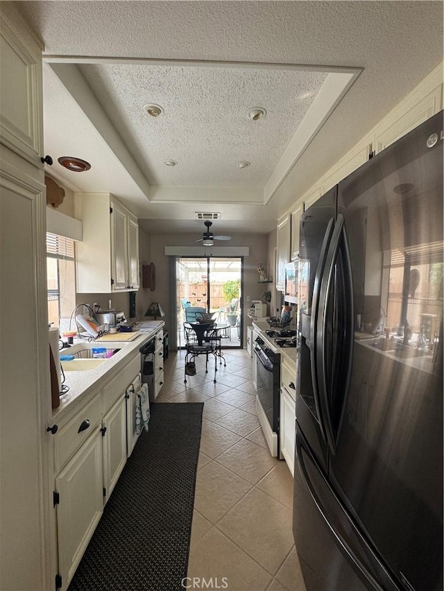 kitchen featuring a tray ceiling, light countertops, a textured ceiling, black appliances, and light tile patterned flooring