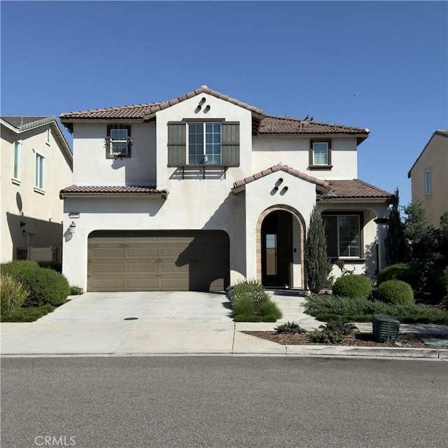 mediterranean / spanish house featuring concrete driveway, a tile roof, an attached garage, and stucco siding