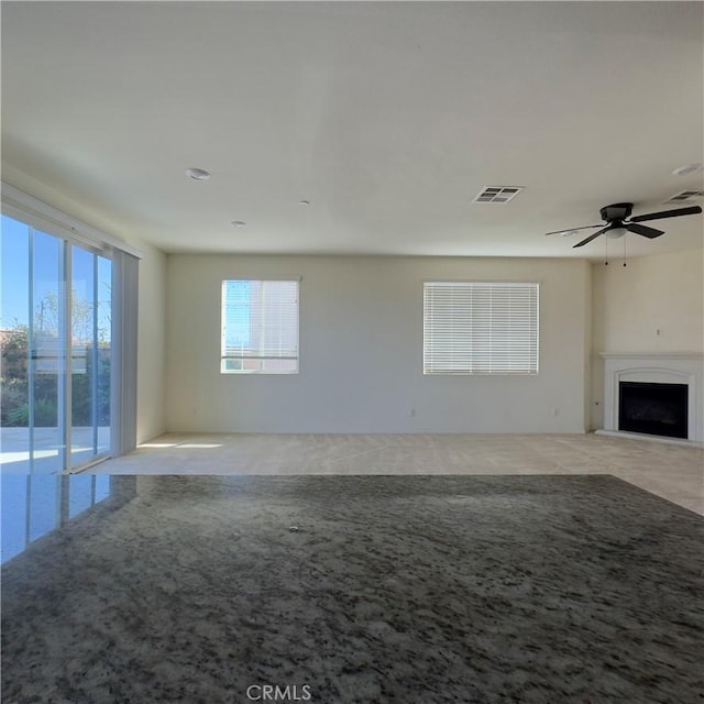 unfurnished living room with a fireplace with raised hearth, carpet, visible vents, and a ceiling fan