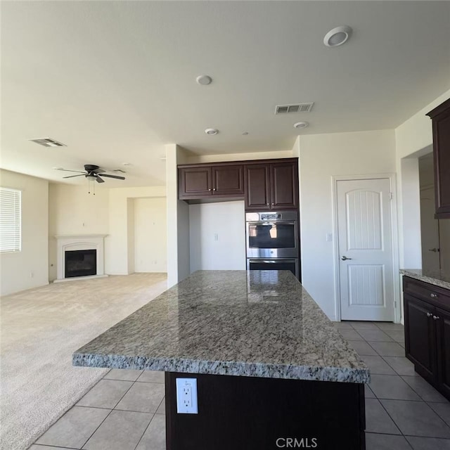 kitchen with a fireplace, light colored carpet, visible vents, double oven, and ceiling fan