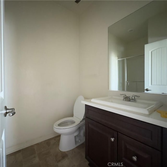 bathroom with vanity, a shower with door, toilet, and baseboards