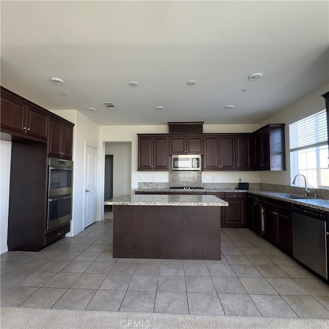 kitchen featuring stainless steel appliances, dark brown cabinetry, visible vents, and a center island