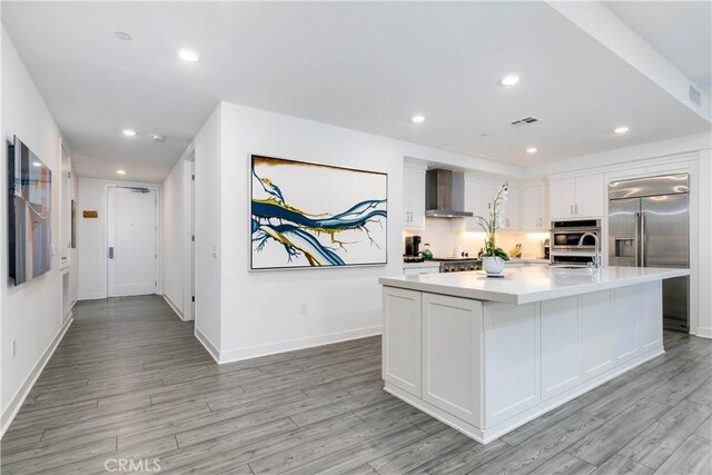 kitchen with recessed lighting, white cabinets, stainless steel appliances, and wall chimney range hood