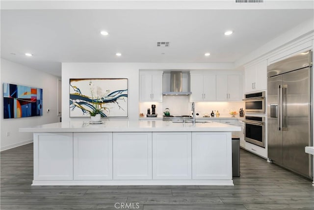 kitchen with a sink, wall chimney range hood, stainless steel appliances, white cabinets, and light countertops