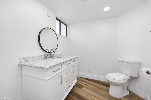 half bath with vanity, wood finished floors, toilet, and baseboards