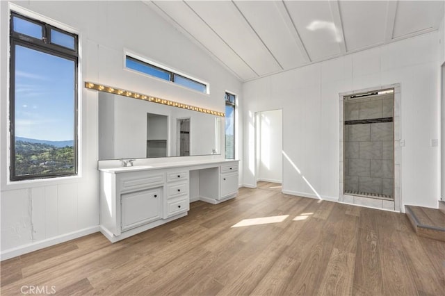 unfurnished bedroom with built in desk, light wood-style flooring, vaulted ceiling, a sink, and baseboards