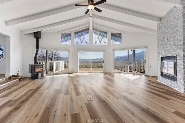 unfurnished living room featuring beam ceiling, a wood stove, a stone fireplace, wood finished floors, and high vaulted ceiling