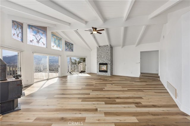 living area with beam ceiling, visible vents, light wood-style flooring, a stone fireplace, and high vaulted ceiling