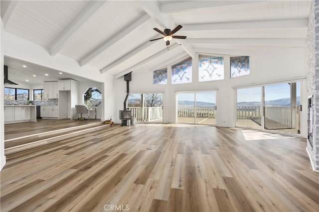 unfurnished living room featuring a wood stove, light wood finished floors, high vaulted ceiling, and beamed ceiling