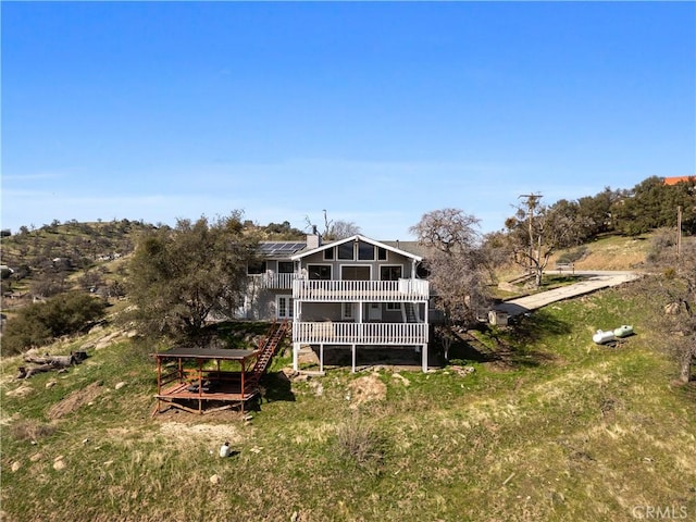 back of house featuring stairs, a chimney, a wooden deck, and roof mounted solar panels