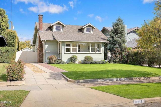 cape cod-style house with a chimney, a shingled roof, a gate, driveway, and a front lawn