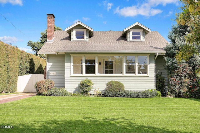 cape cod-style house featuring a shingled roof, a chimney, and a front yard