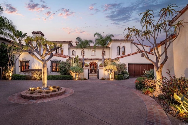 mediterranean / spanish house with a garage, curved driveway, and stucco siding