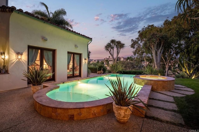 pool at dusk with an outdoor pool and an in ground hot tub