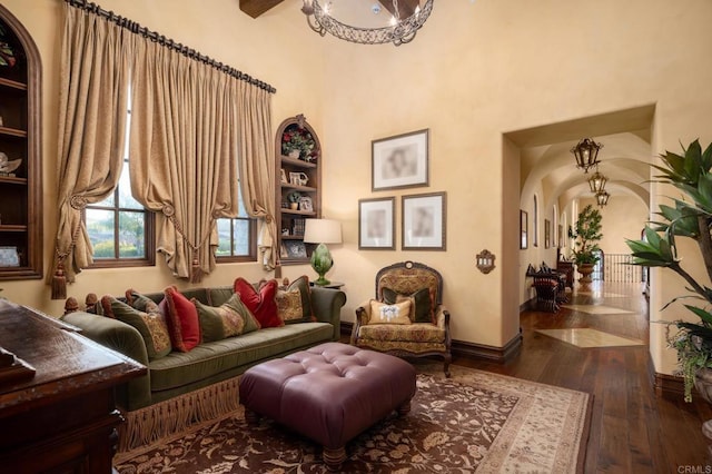 living area featuring dark wood-style floors, arched walkways, a notable chandelier, and baseboards