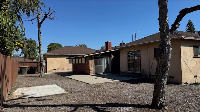 rear view of house with a patio, a chimney, stucco siding, crawl space, and fence