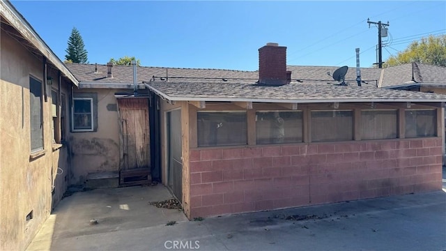 view of exterior entry featuring a shingled roof and a chimney