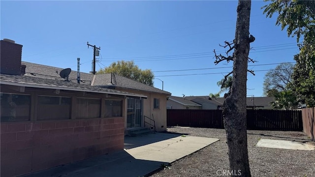 rear view of house with entry steps, a fenced backyard, a chimney, and a patio