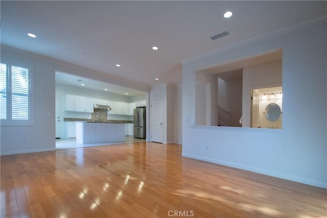 unfurnished living room featuring light wood-style flooring, a sink, visible vents, and baseboards