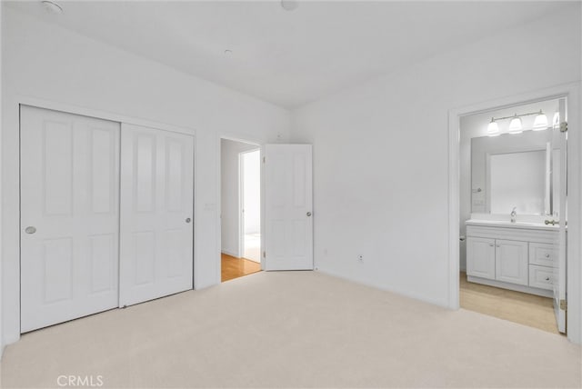 unfurnished bedroom featuring light carpet, a closet, a sink, and connected bathroom